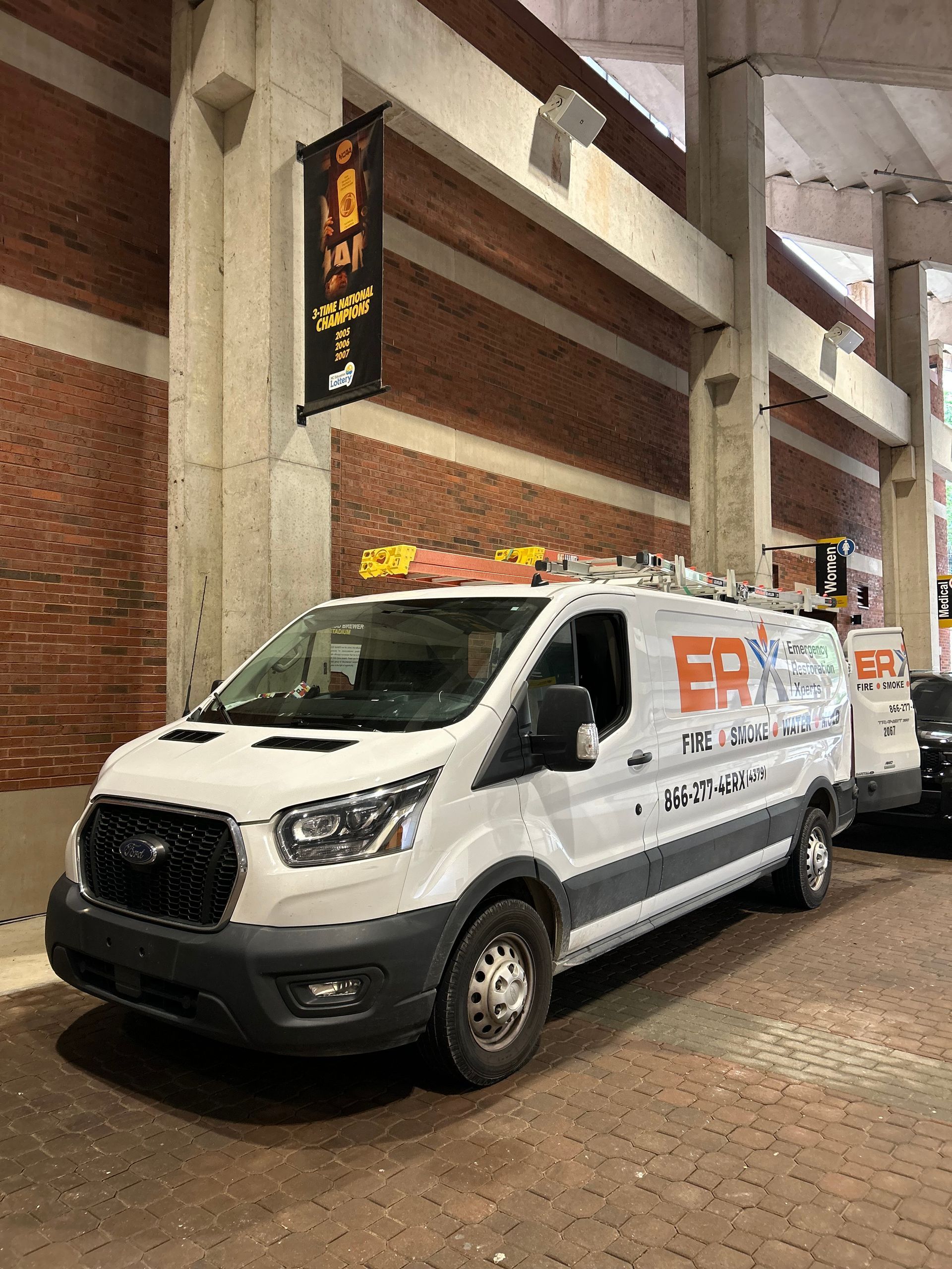 White utility van parked outside a brick building entrance with a hanging sign.