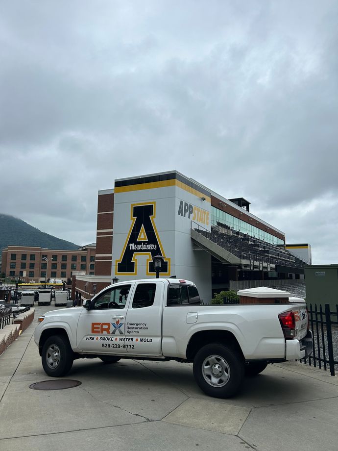White pickup truck parked beside a building with a large black-and-gold “A” on the wall.