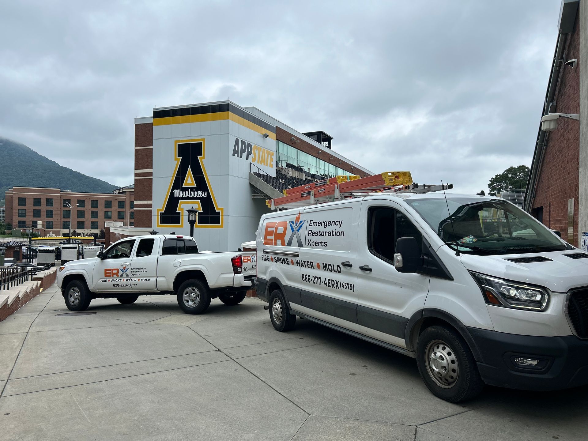 White utility vans parked beside a large building with a bold yellow-and-black “A” mural on a cloudy day