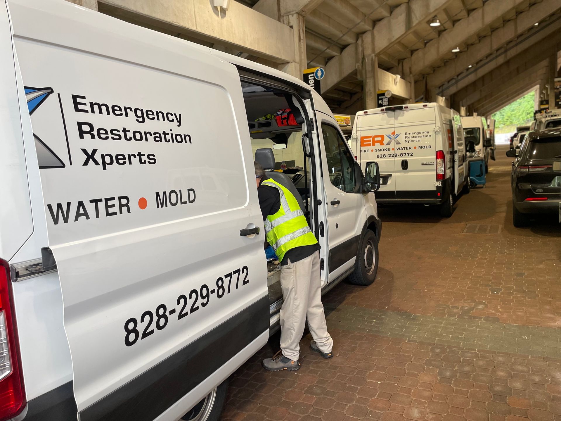 Workers outside water damage restoration vans under a covered building entryway