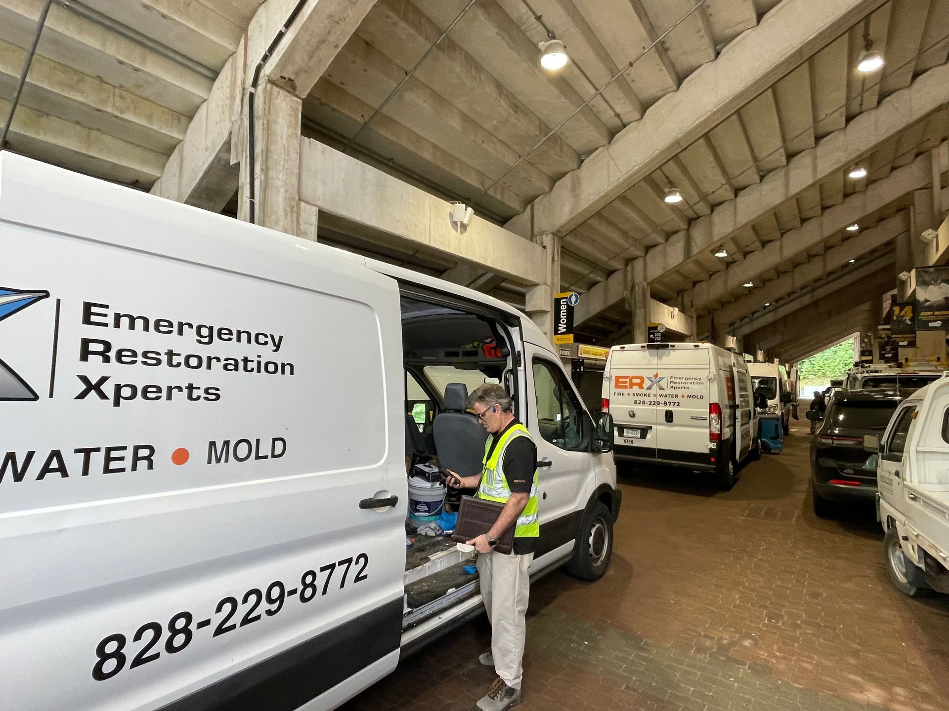 Restoration company vans parked in an industrial garage; worker in safety vest stands by a van.