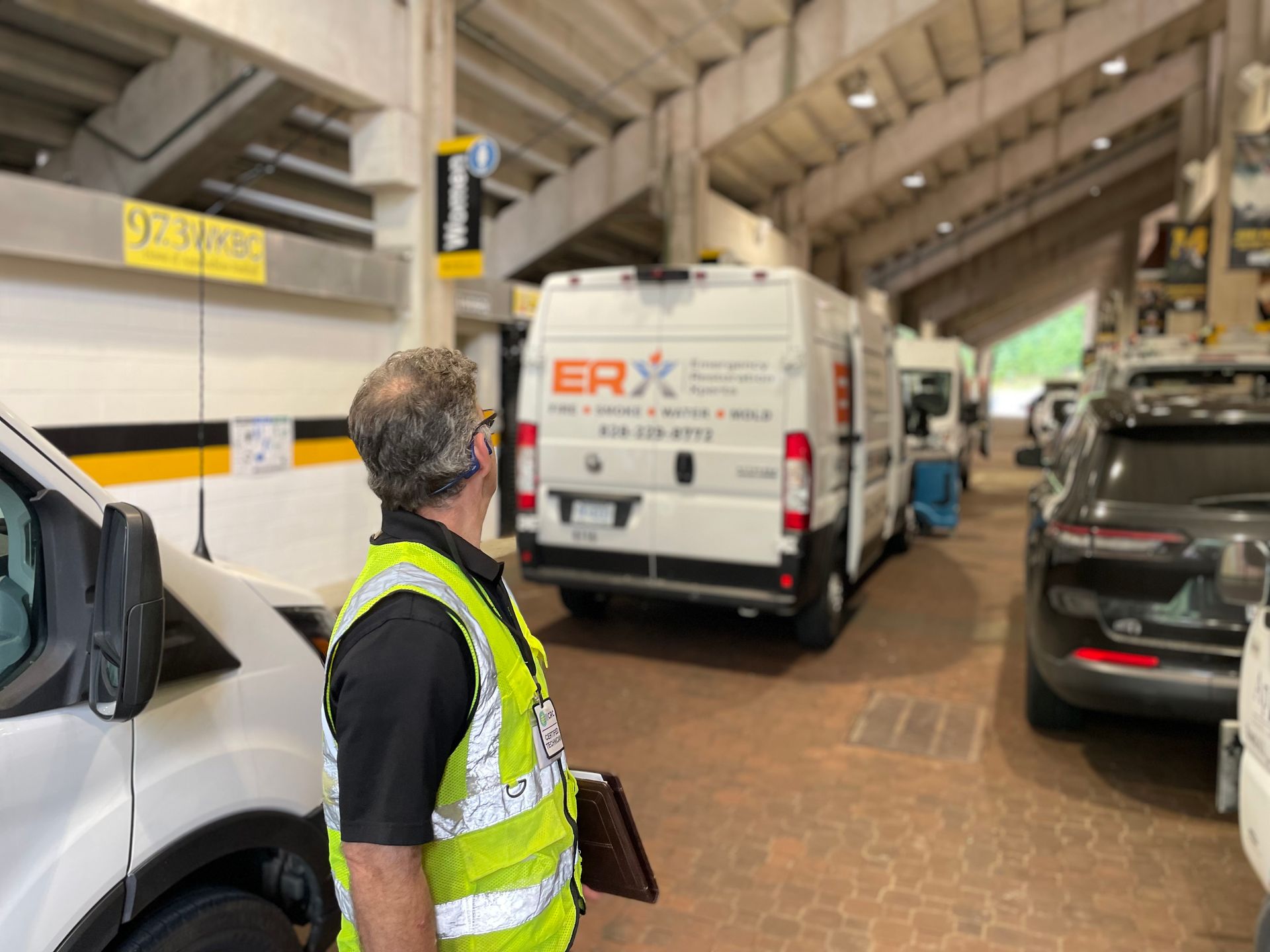 Worker in yellow vest standing in a parking garage beside white and black vans.