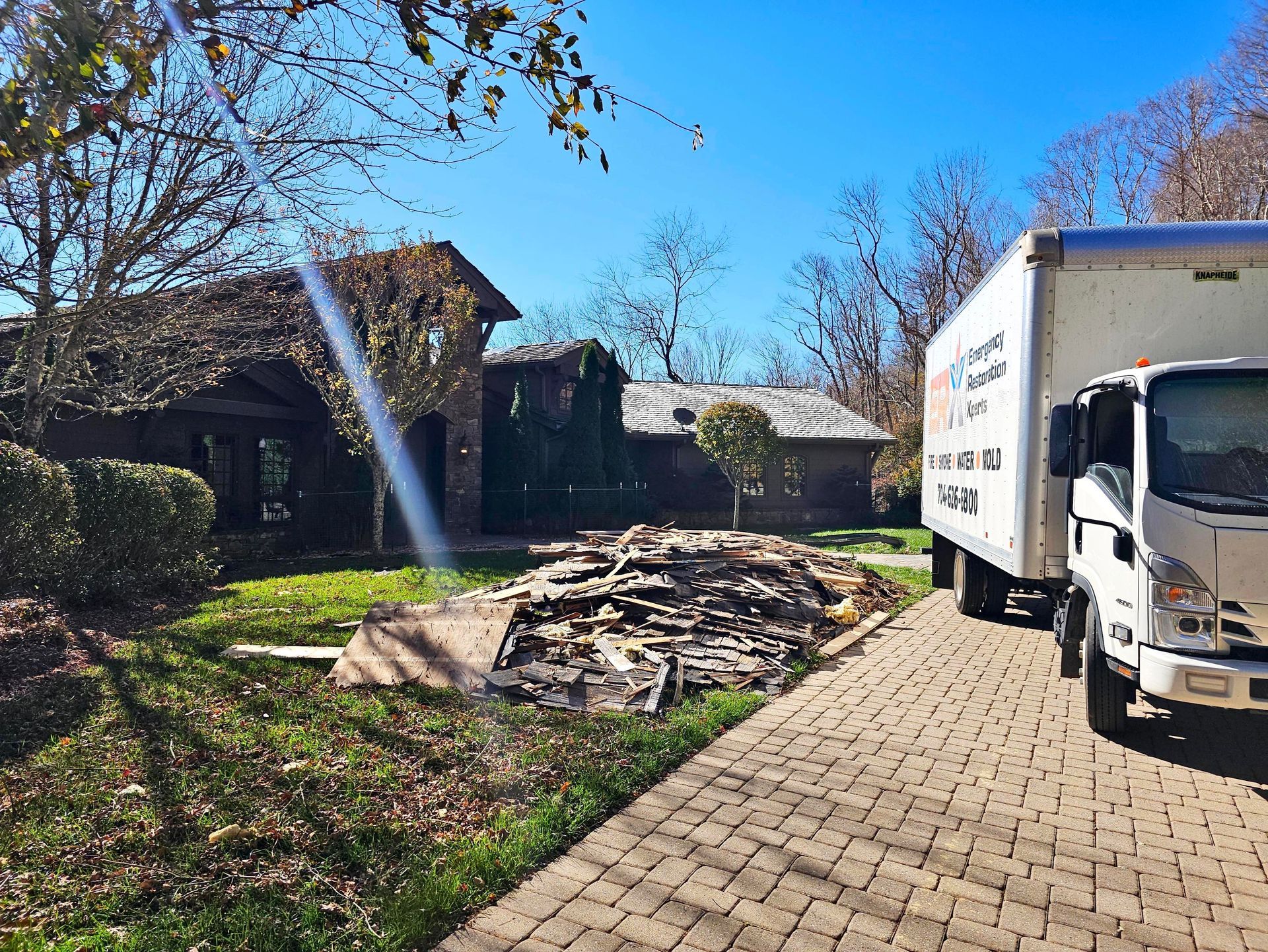 Moving truck parked by a house with debris in the yard and a sprinkler spraying water nearby