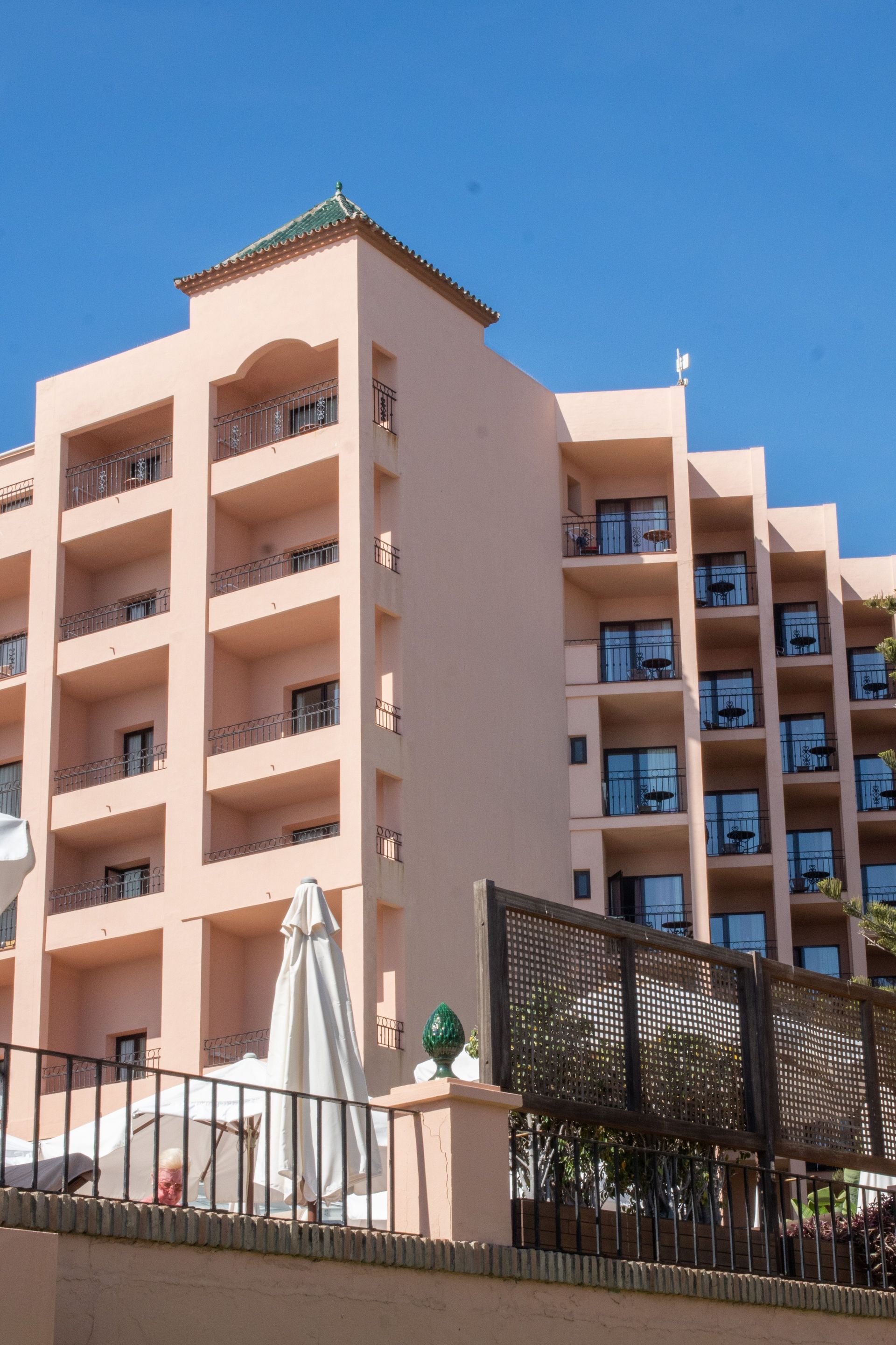 Pink resort building with balconies and green roof against a clear blue sky