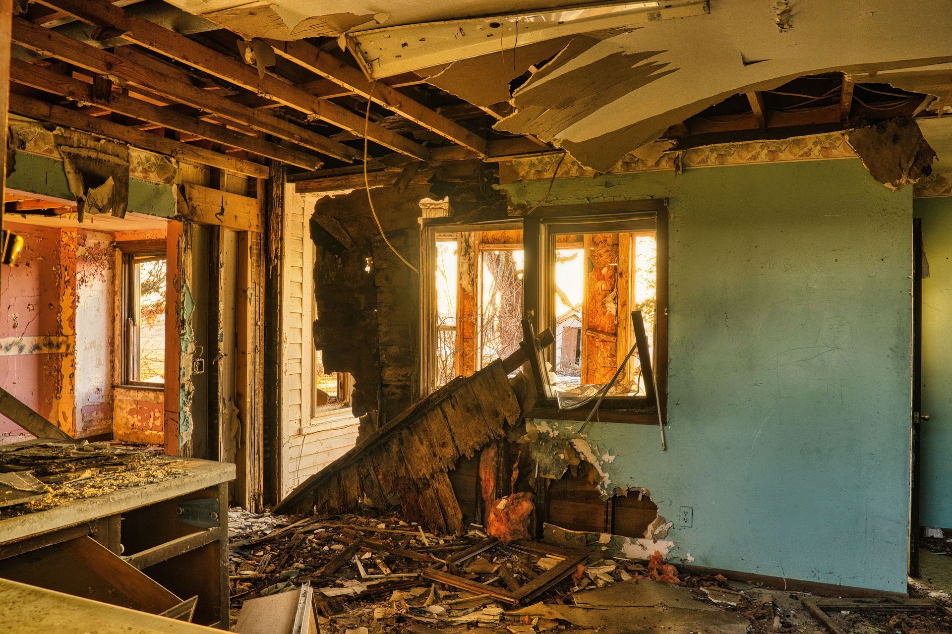 Dilapidated room with collapsed ceiling, broken windows, and debris scattered across the floor.