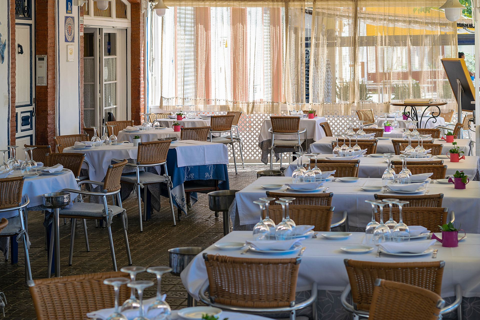Outdoor café dining area with white-clothed tables and wicker chairs under a sunlit canopy