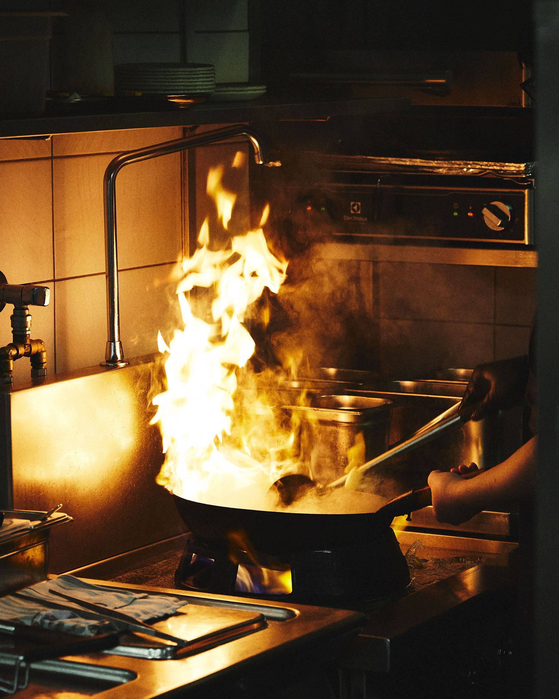 Kitchen pan fire with large flames rising from a stovetop, a hand nearby holding the pan