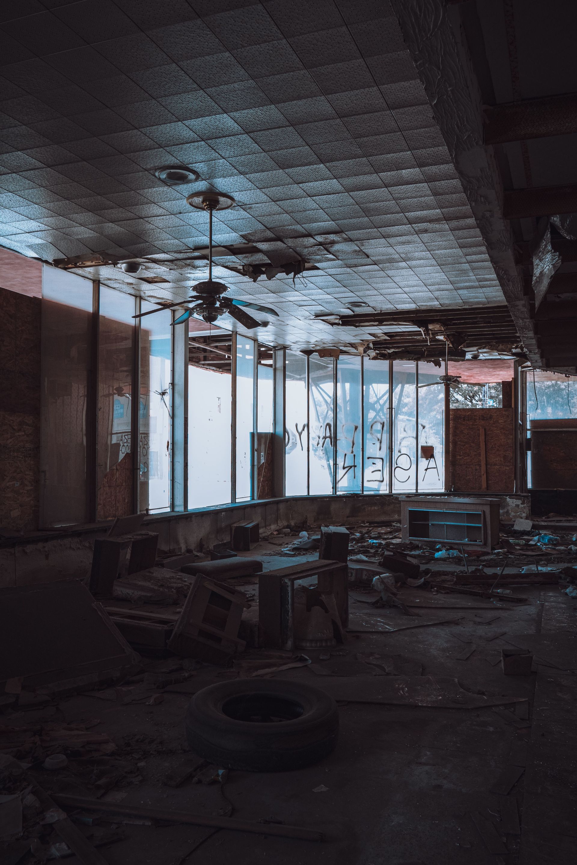 Abandoned, dark room with broken furniture, tires, and bright windows along the wall