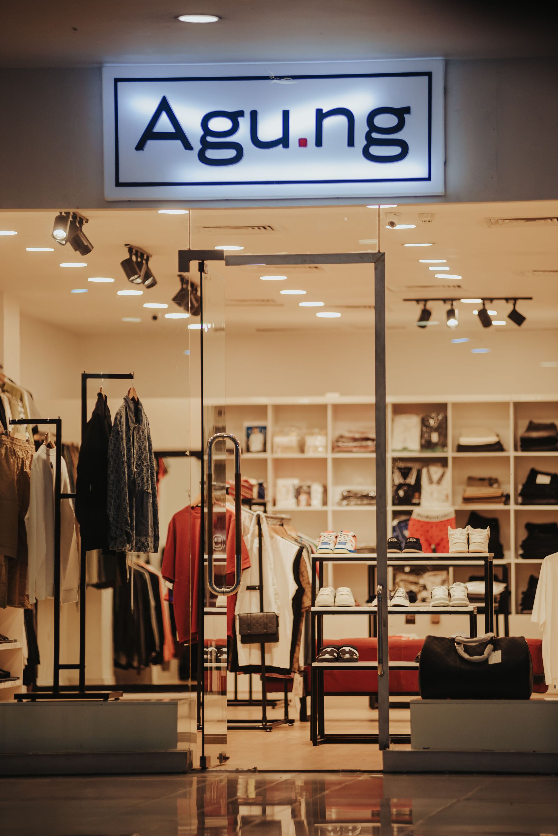 Clothing store interior with a lit “Agu.ng” sign above racks, shelves, and displays