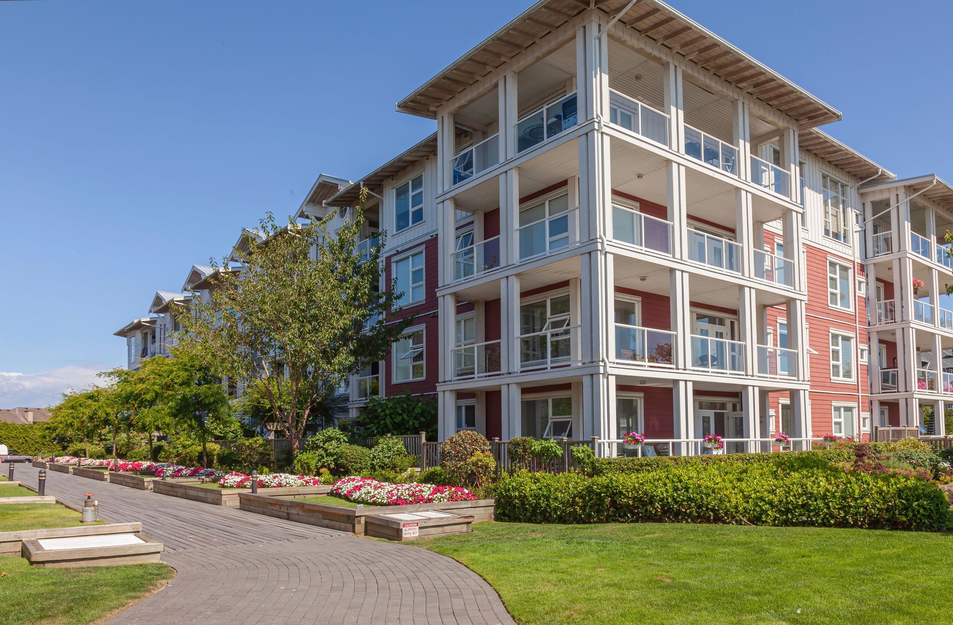 Modern apartment building with balconies, landscaped garden, and walkway under a blue sky