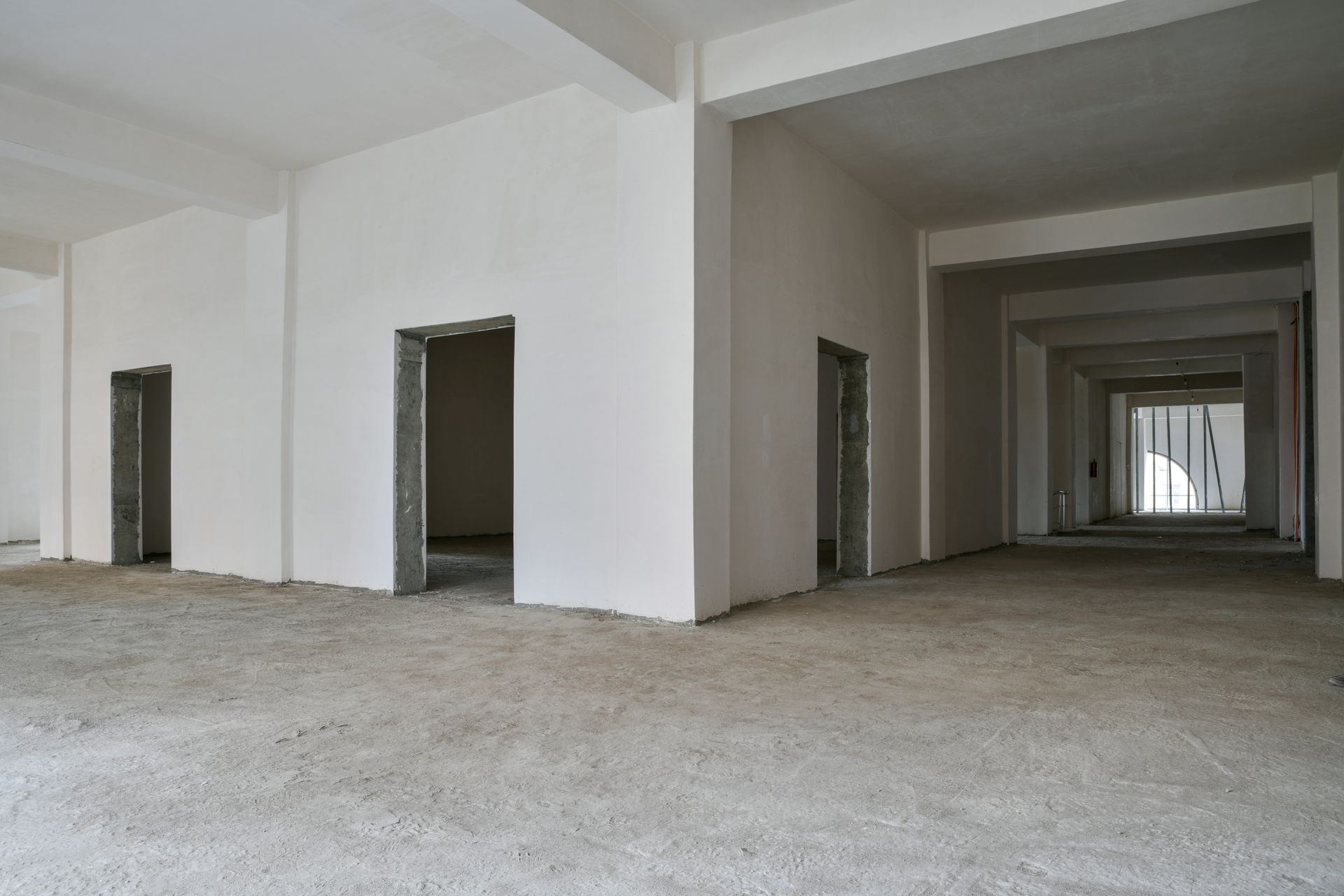 Empty unfinished interior with multiple doorways and a rough concrete floor, receding into the distance