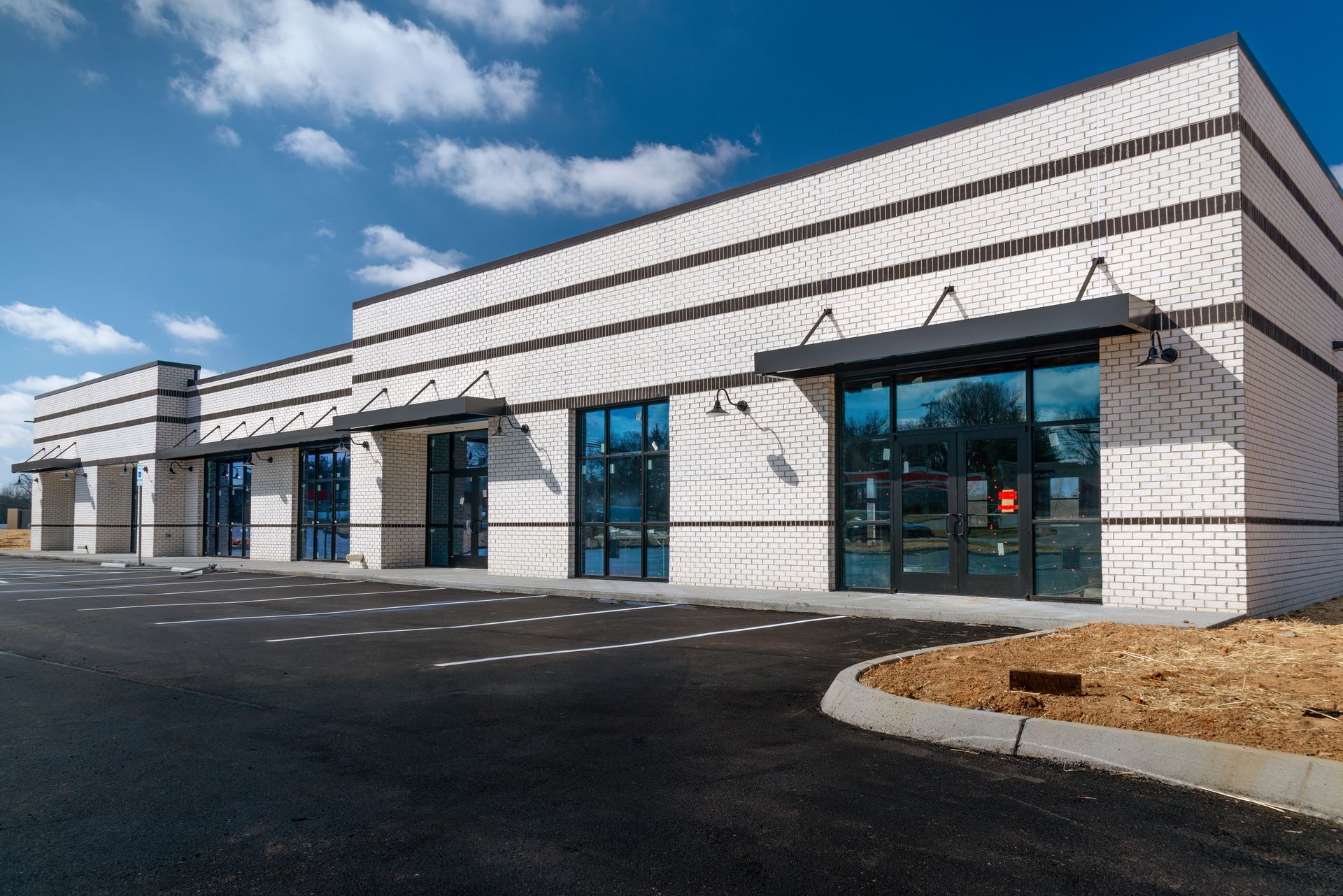 Modern white commercial building with large windows and a parking lot under a blue sky