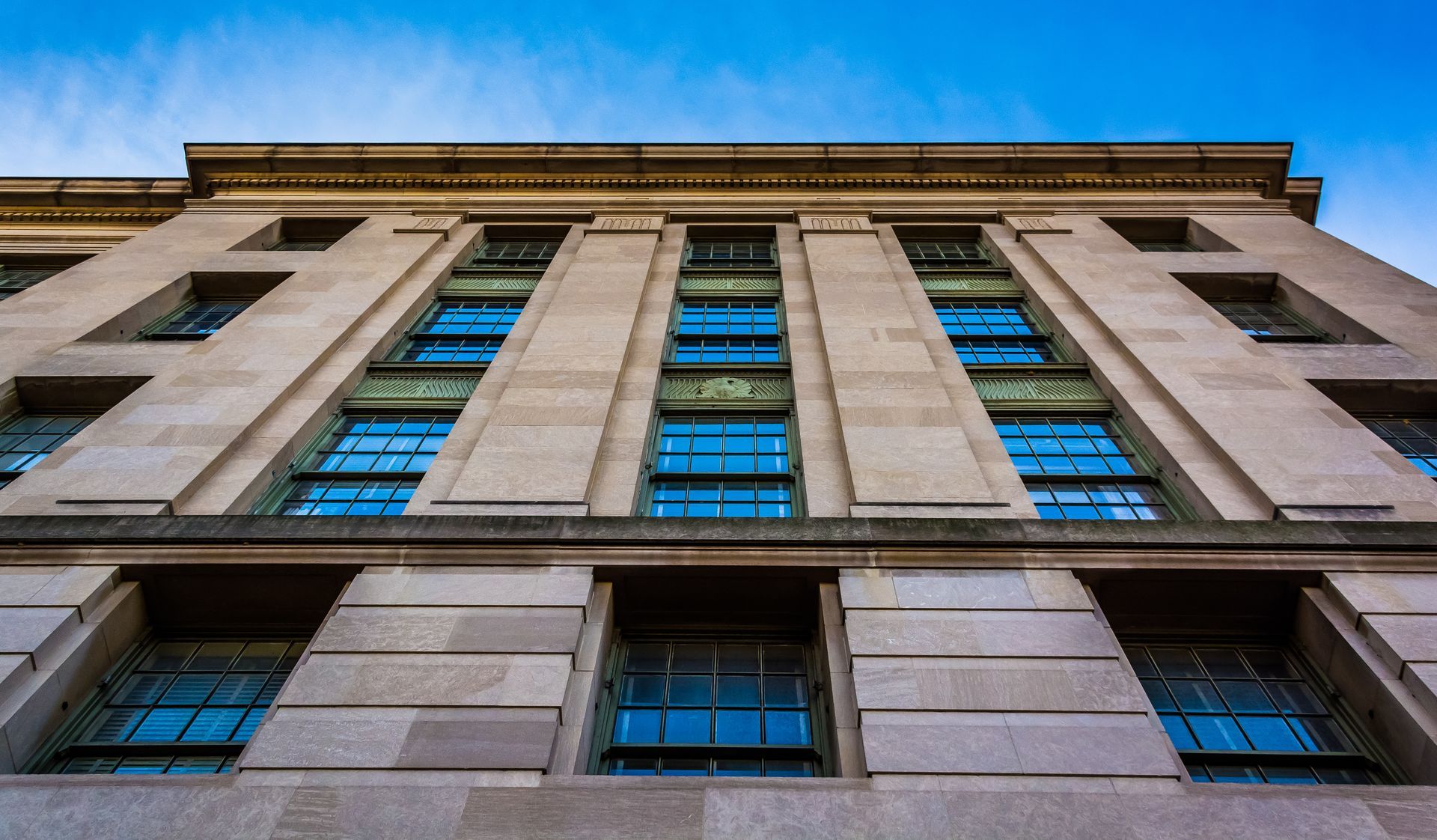 Low-angle view of a stone office building facade with tall blue-tinted windows and beige columns