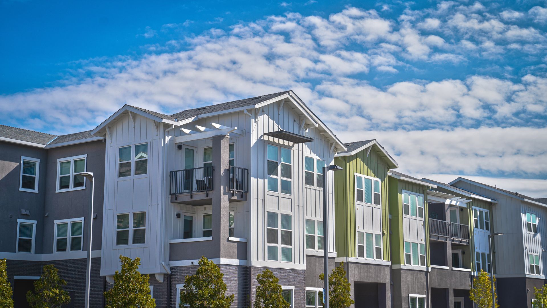 Modern apartment building with gray, white, and green facades under a partly cloudy blue sky