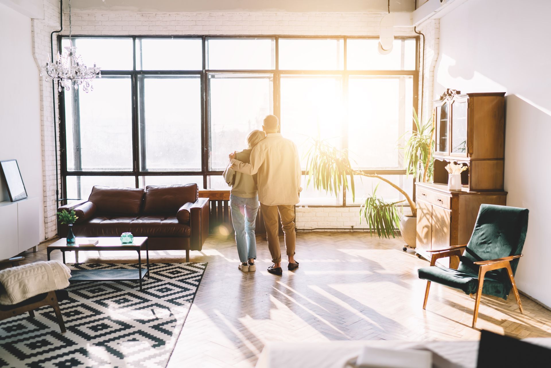 Two people in a bright loft living room with large windows, sofas, and a patterned rug
