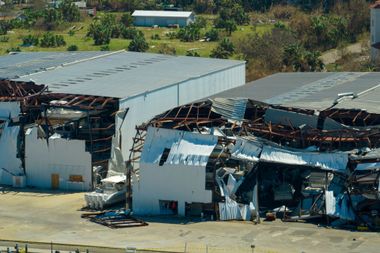 Damaged warehouse buildings with collapsed roofs and twisted metal after a storm or disaster