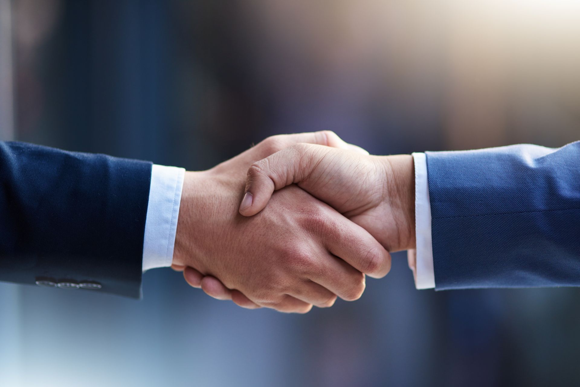 Two people in blue suits shaking hands in a close-up business deal