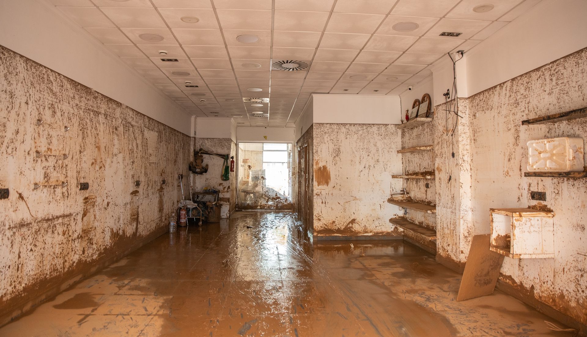 Flood-damaged room with muddy floor, peeling walls, and debris scattered inside.