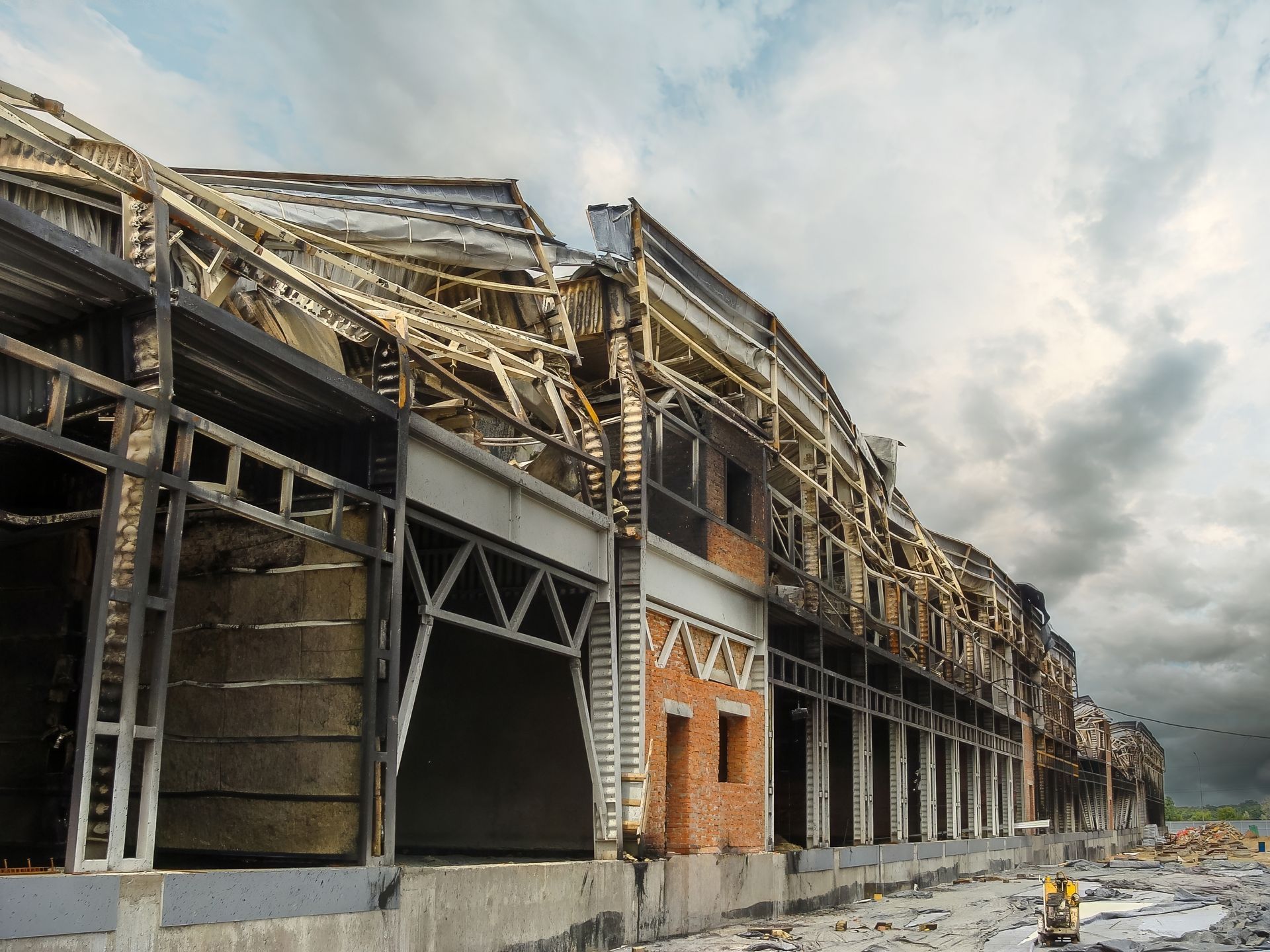Partially destroyed building with collapsed roof and exposed steel beams under a cloudy sky