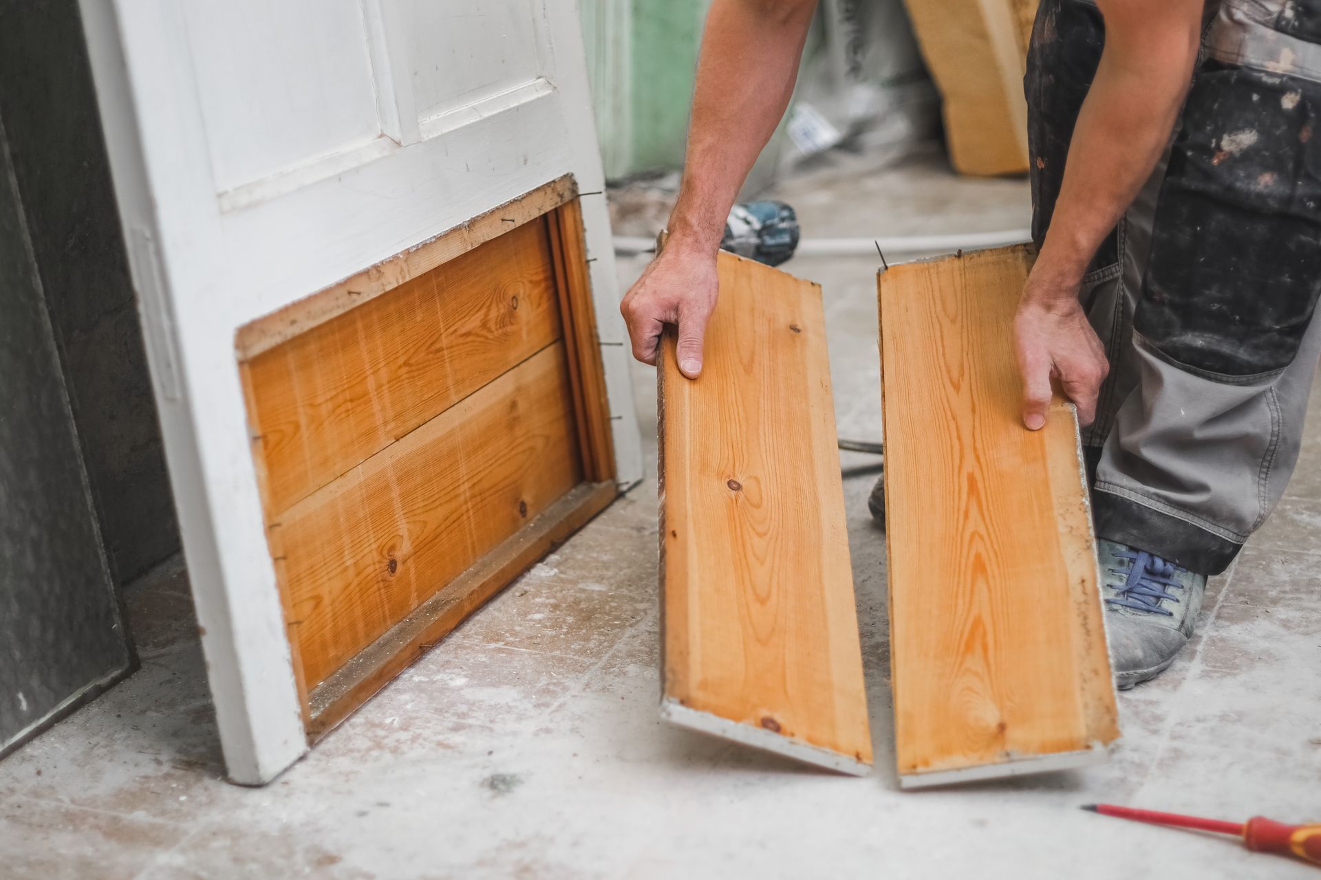 Worker holding two wooden cabinet doors beside a damaged door panel during repair work