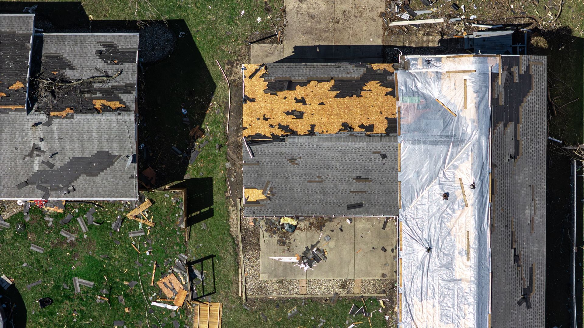 Aerial view of several rooftops with damaged shingles and a white tarp covering one roof.