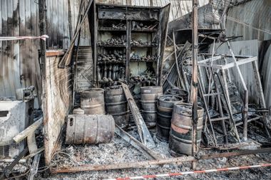 Charred storage area with barrels, shelves, and debris after a fire