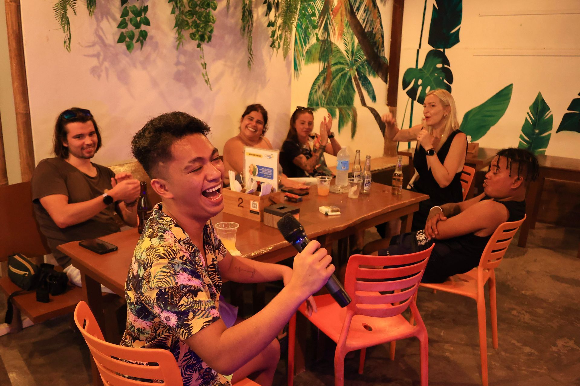 Five people singing into a microphone, laughing in a karaoke setting.