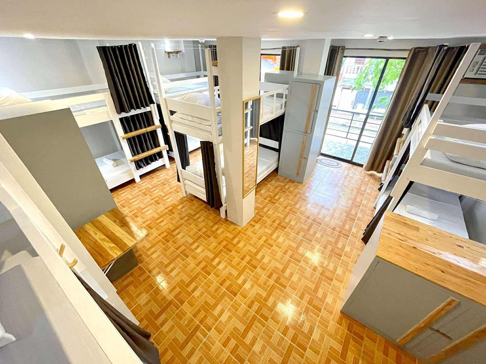 Bunk beds in a brightly lit hostel room, with tiled floors and a sliding door to a balcony.