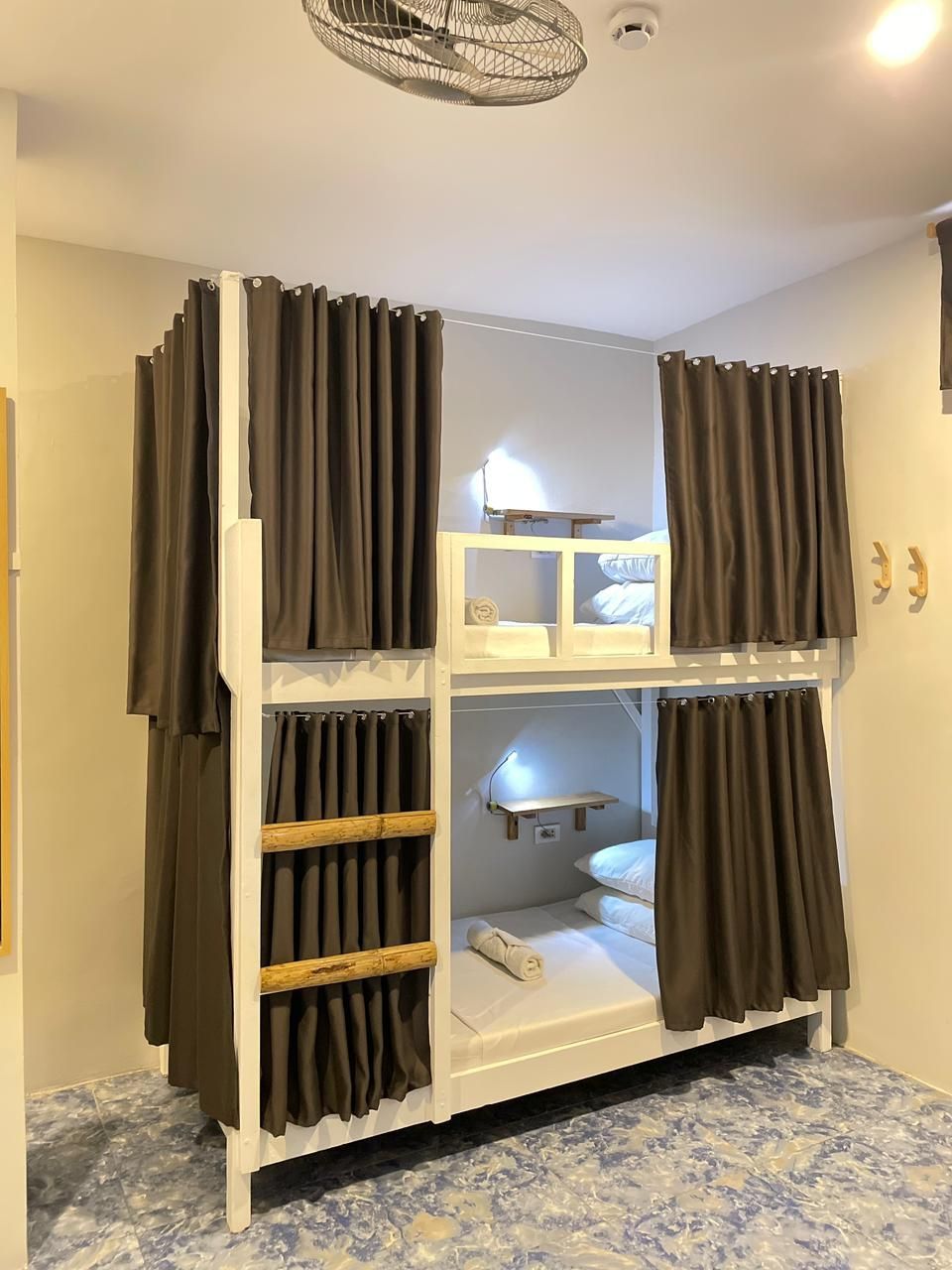 Bunk beds in a room, each bed draped with brown curtains. A ceiling fan is visible.