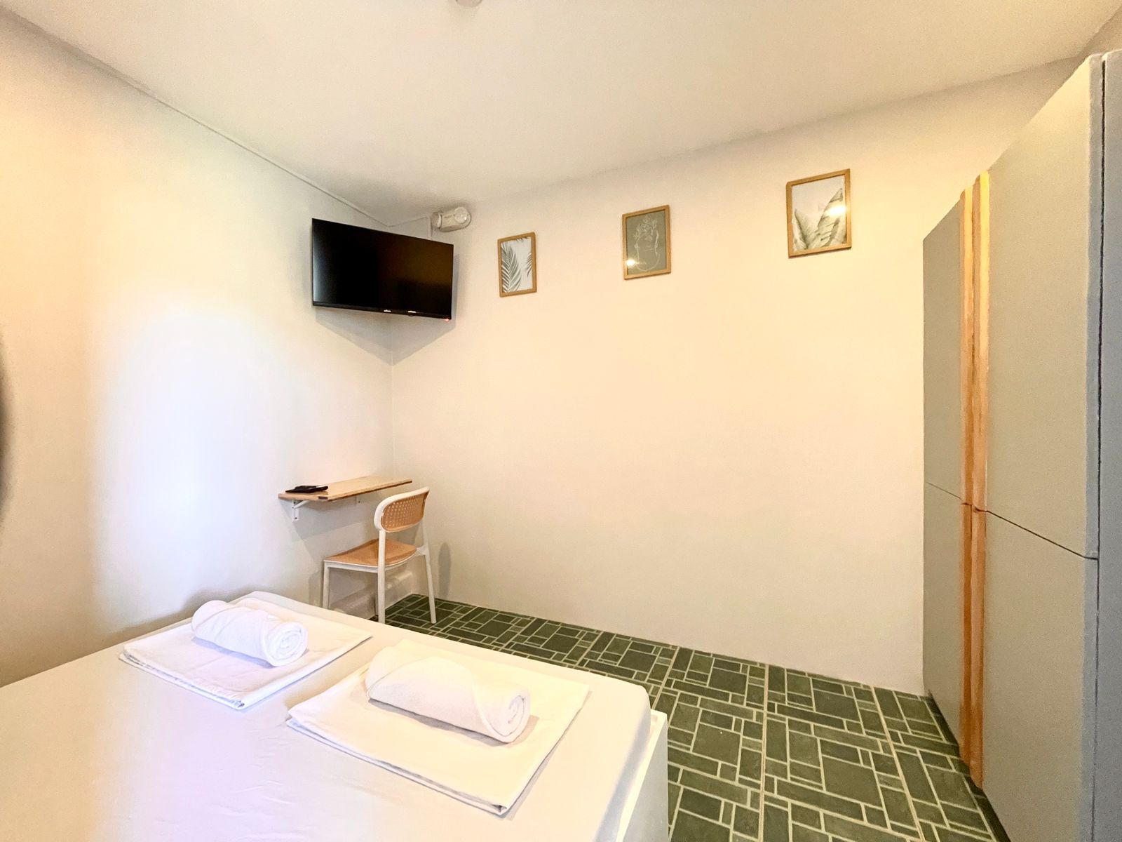 Bedroom with bed, desk, TV, and closet. Green tiled floor, white walls, and framed art.