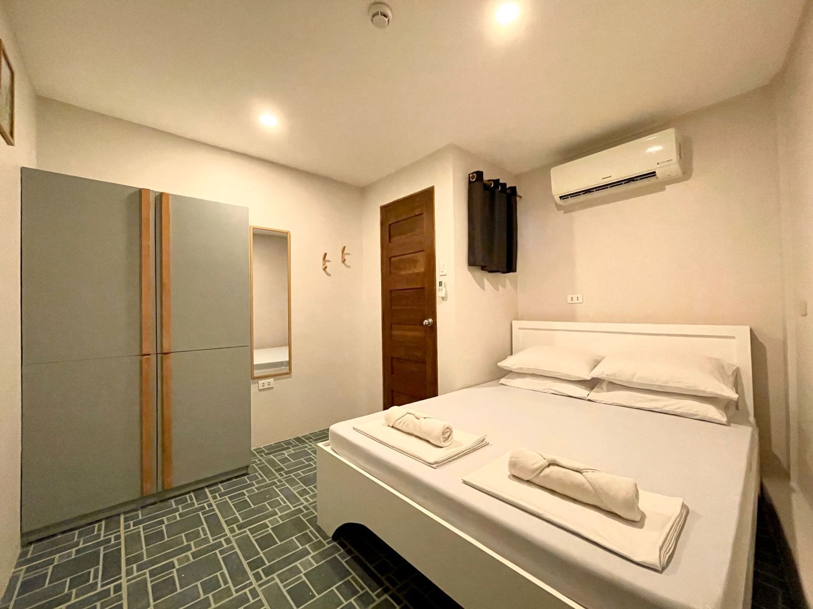 Bedroom with a white bed, gray wardrobe, and air conditioner. Floor is blue and white patterned.