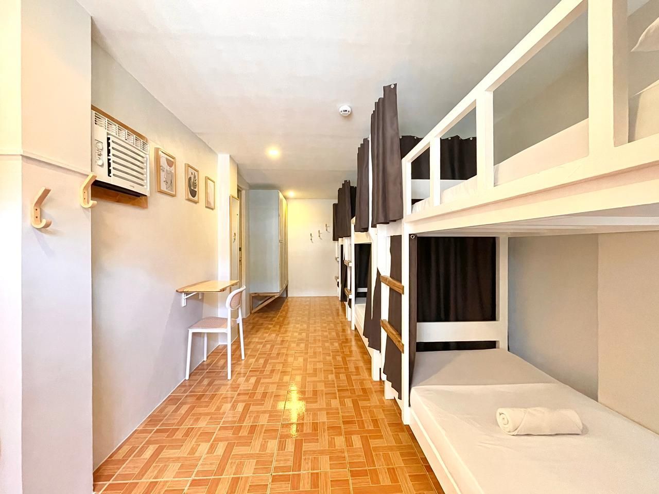 Bunk beds line a narrow hostel room with a desk and tiled floor.