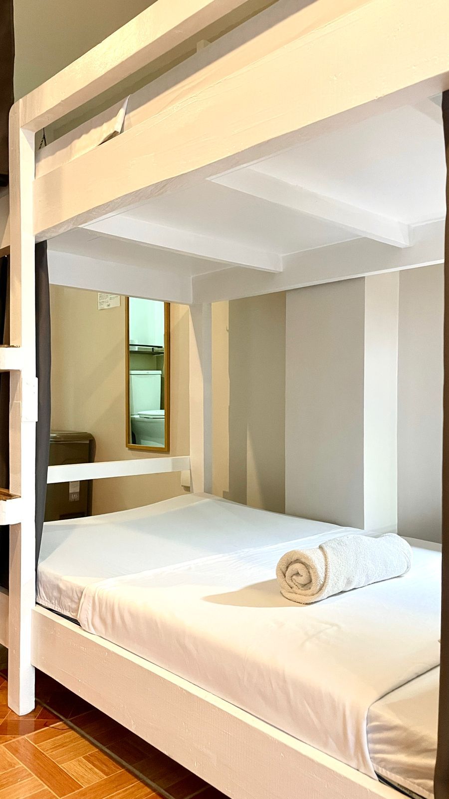 White bunk bed in a room, with a rolled towel on the bottom bunk. A mirror is visible in the background.