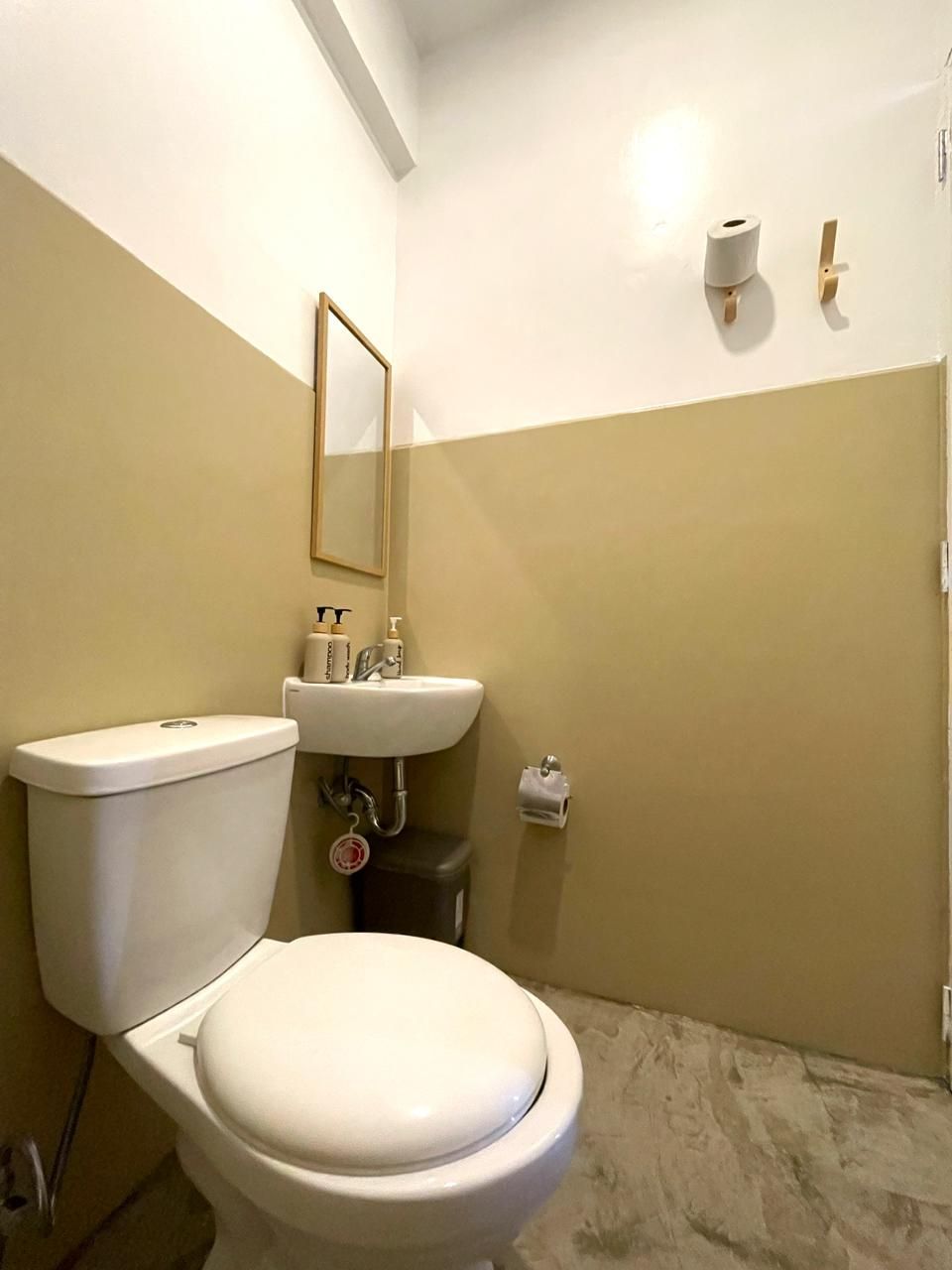 Small bathroom with a white toilet and sink; beige and white walls, wood-framed mirror.