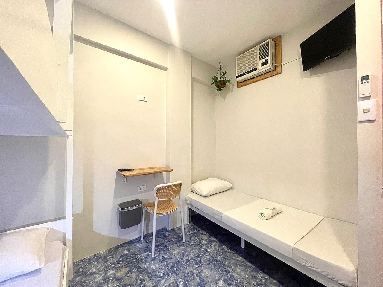 Small hostel room with bunk beds, single bed, desk, TV, and air conditioner.