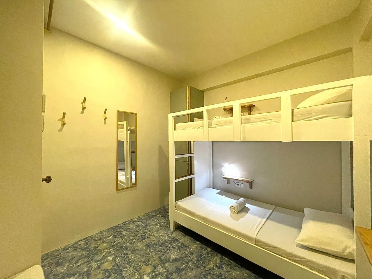 Bunk beds in a room. White beds against a light-yellow wall. Blue and gray patterned flooring.