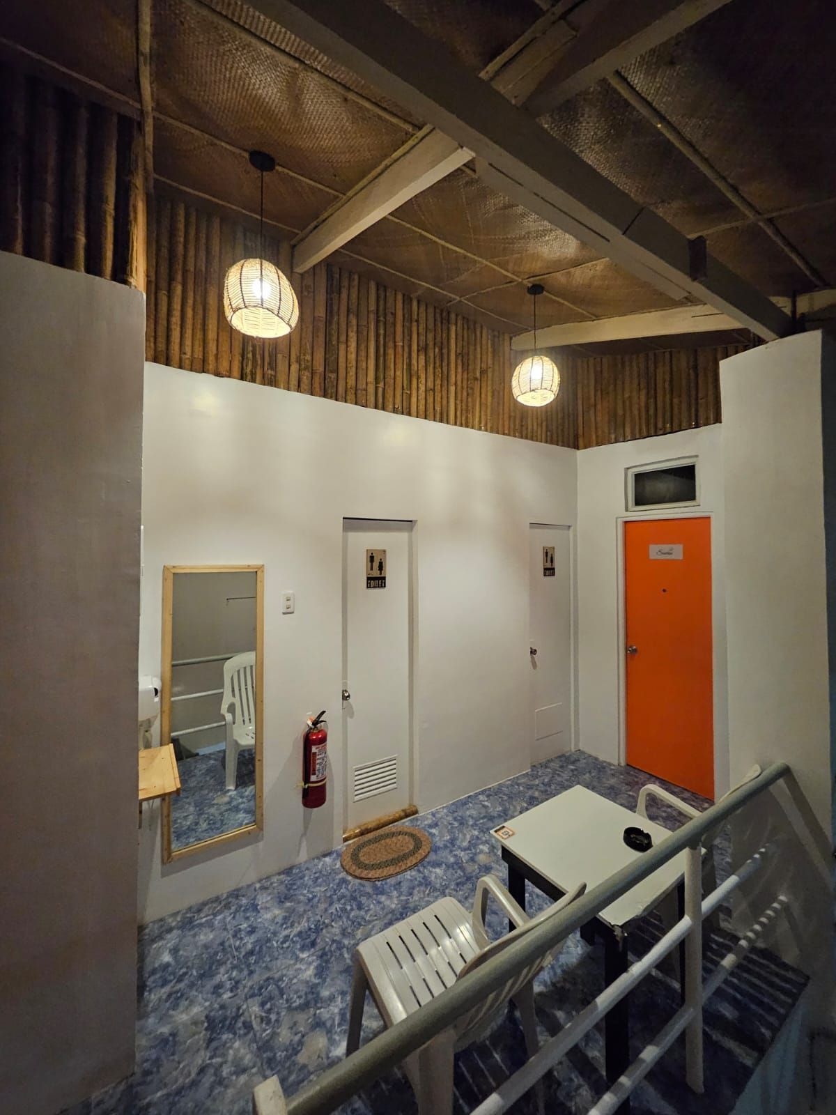 Interior view of a small room. White walls, bamboo ceiling, blue tile floor, two pendant lights.