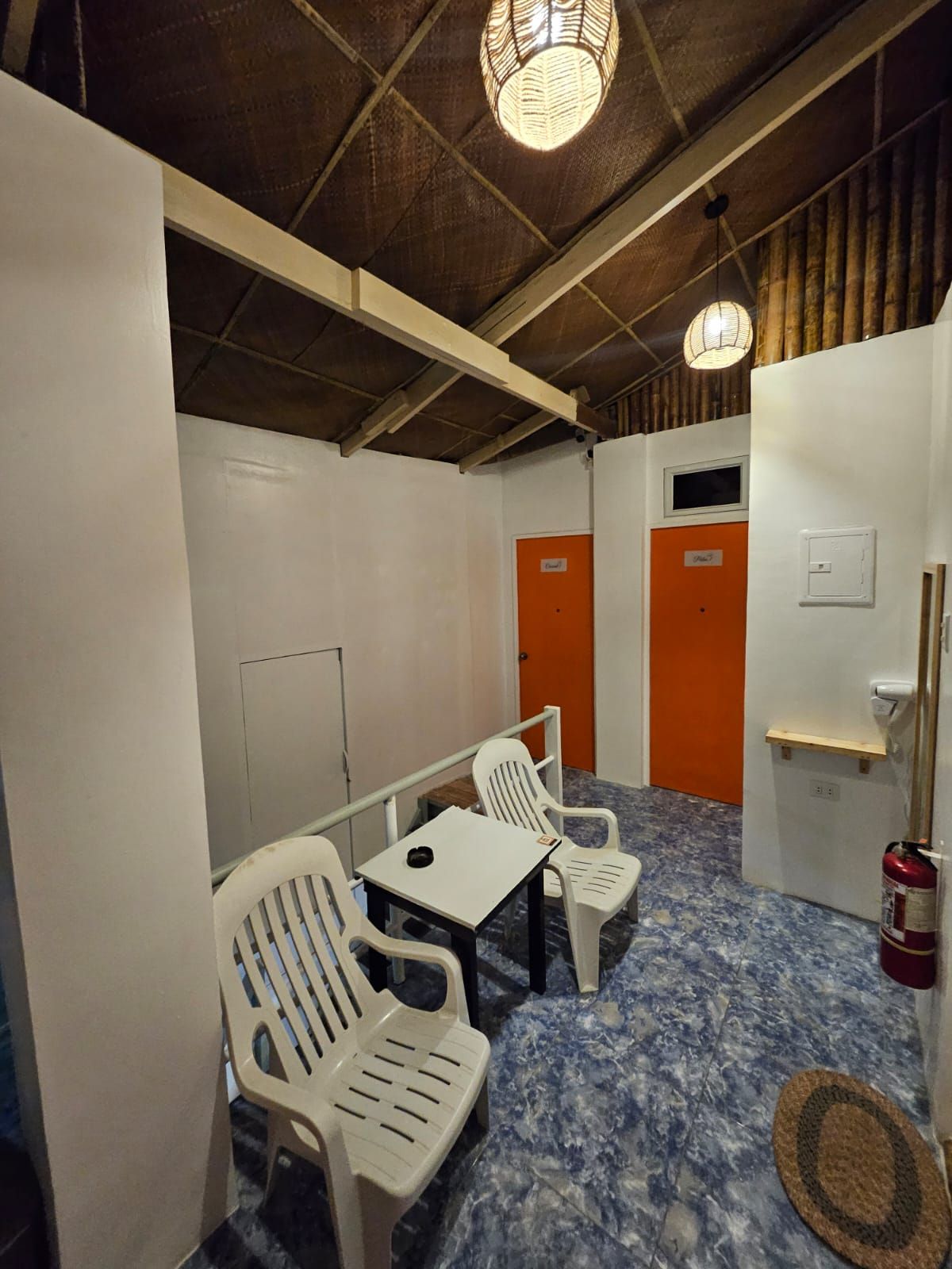 Small indoor space with white walls, blue tiled floor, plastic chairs, and two orange doors.