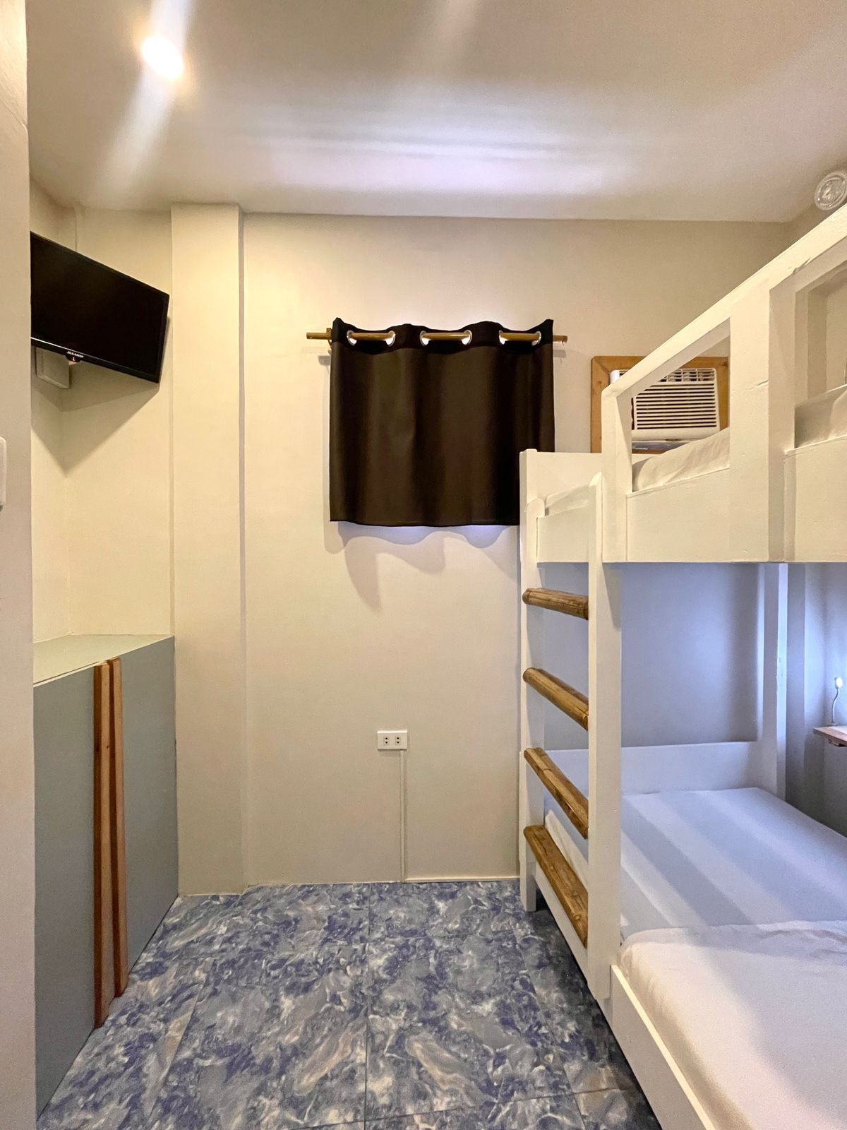 Bunk beds in a small room with a window, TV, and blue tiled floor.