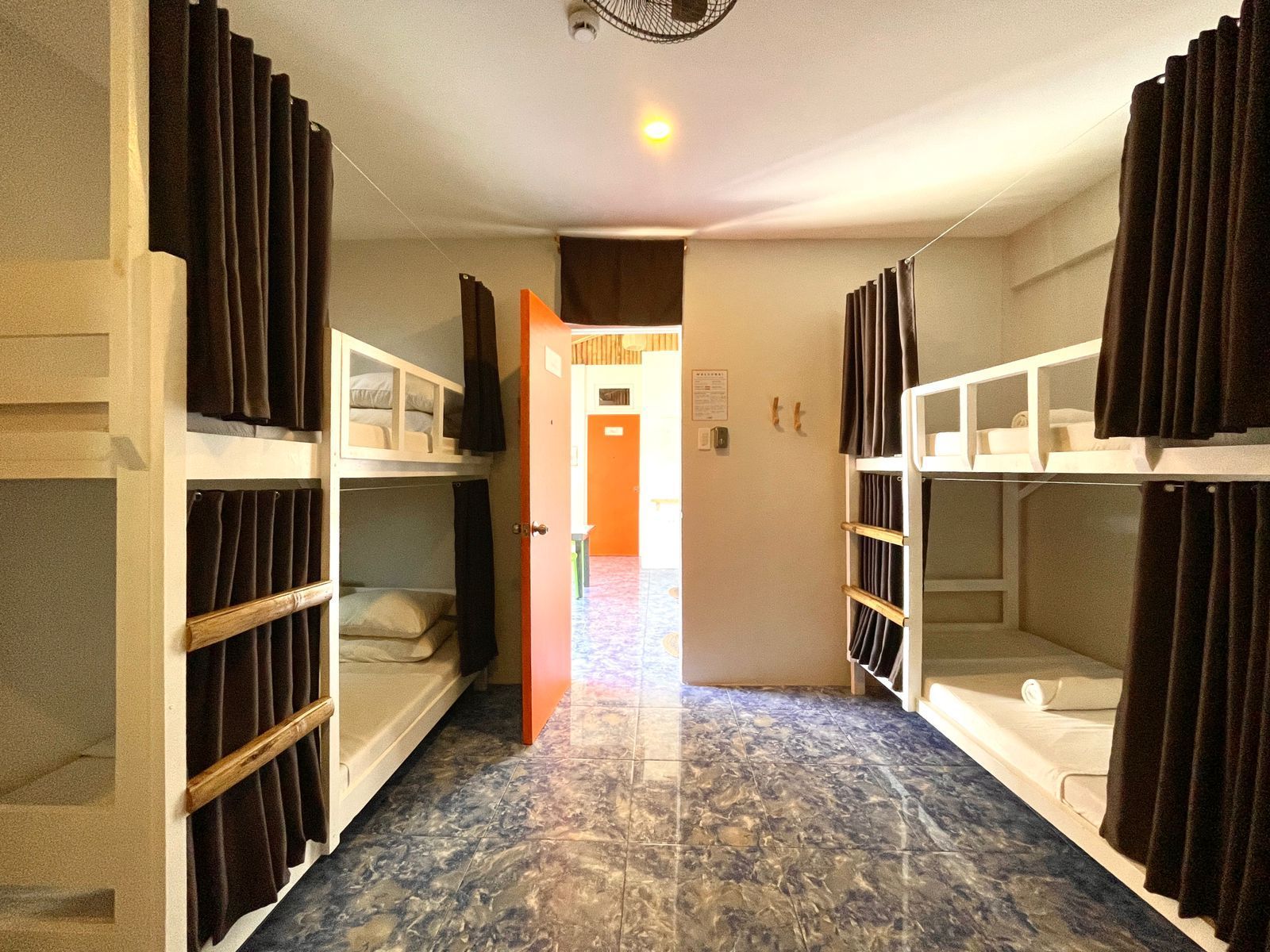 Bunk bed hostel room with brown curtains, orange door, and blue tiled floor.