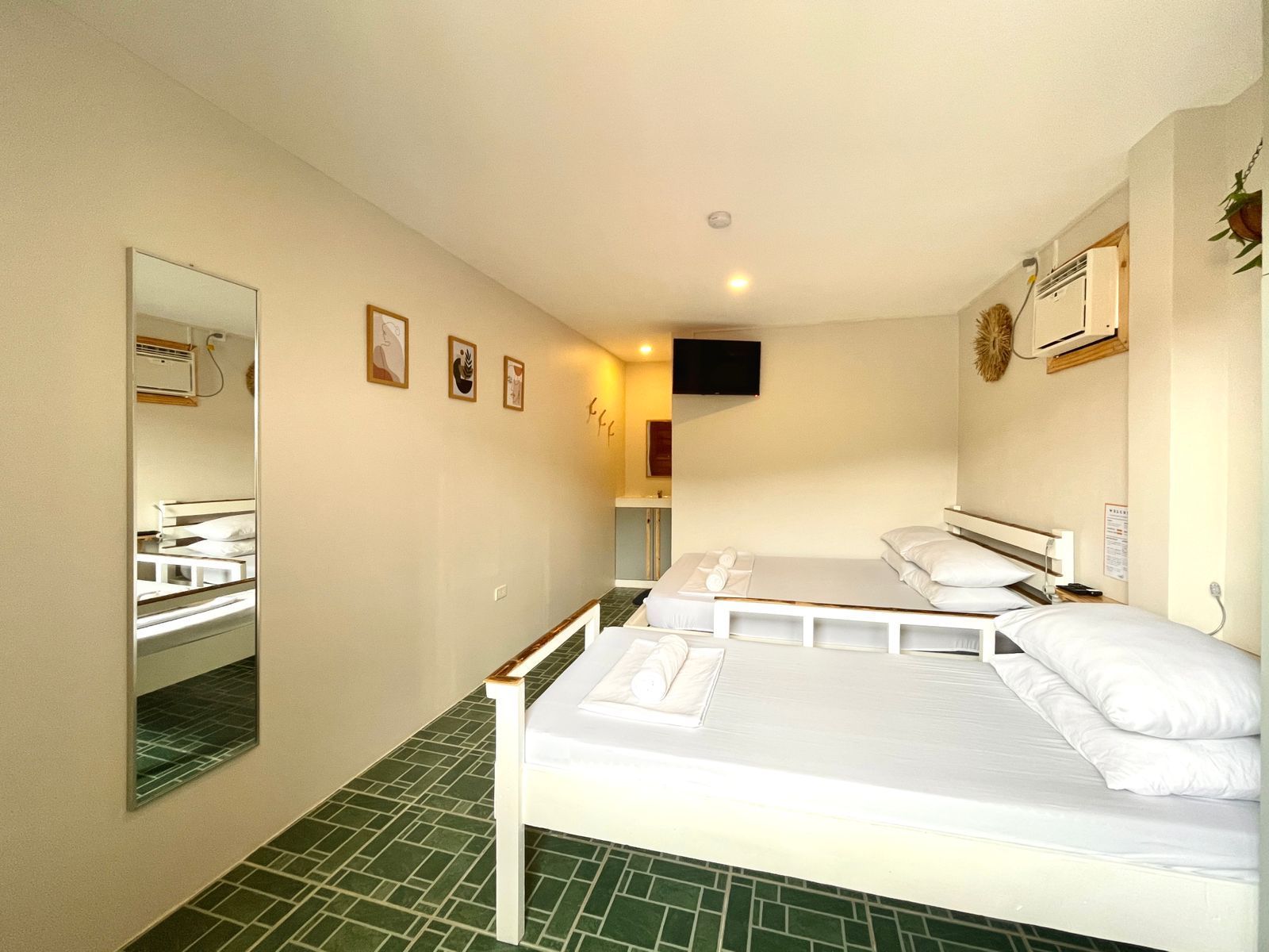 A small hotel room with two beds, a mirror, and a small TV. White walls and bedding.
