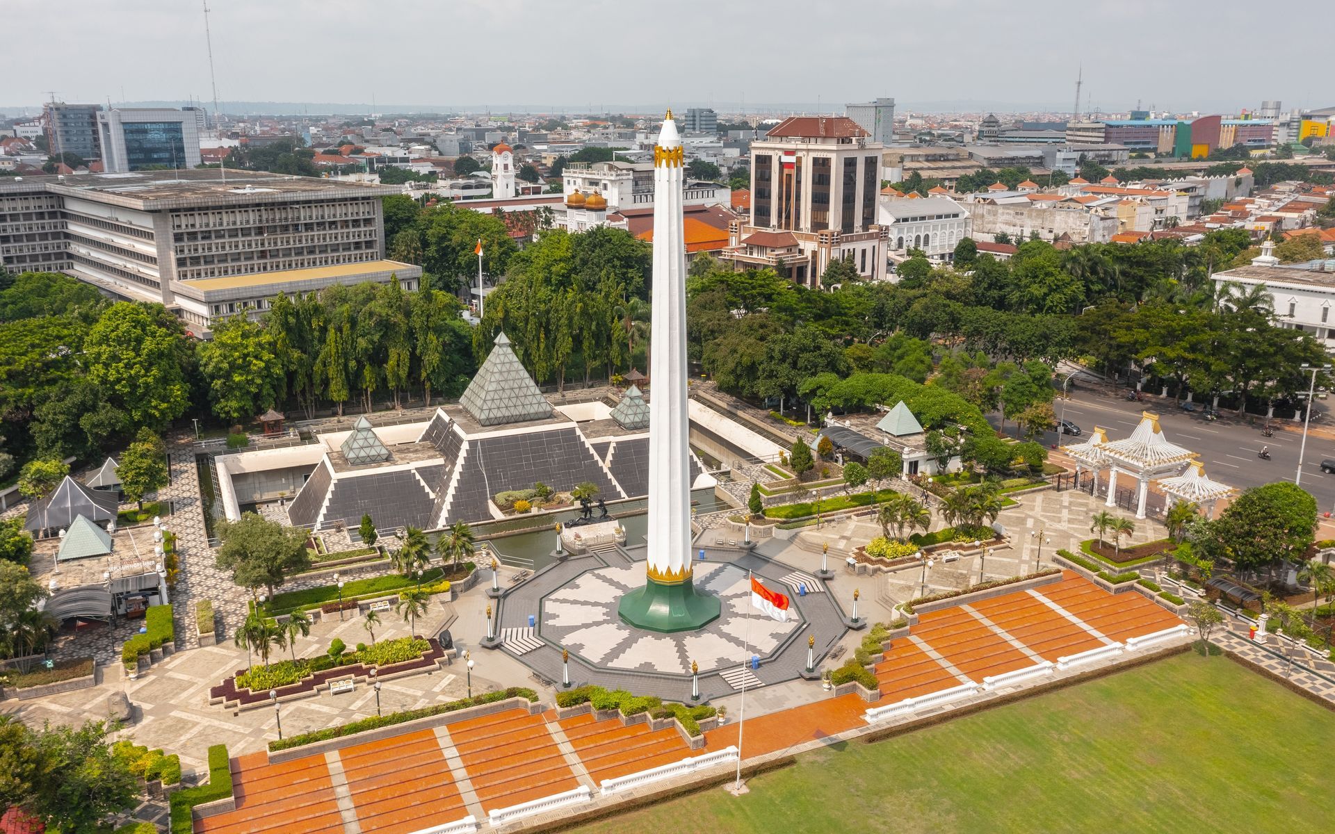 Monument in a city square, surrounded by buildings and greenery.