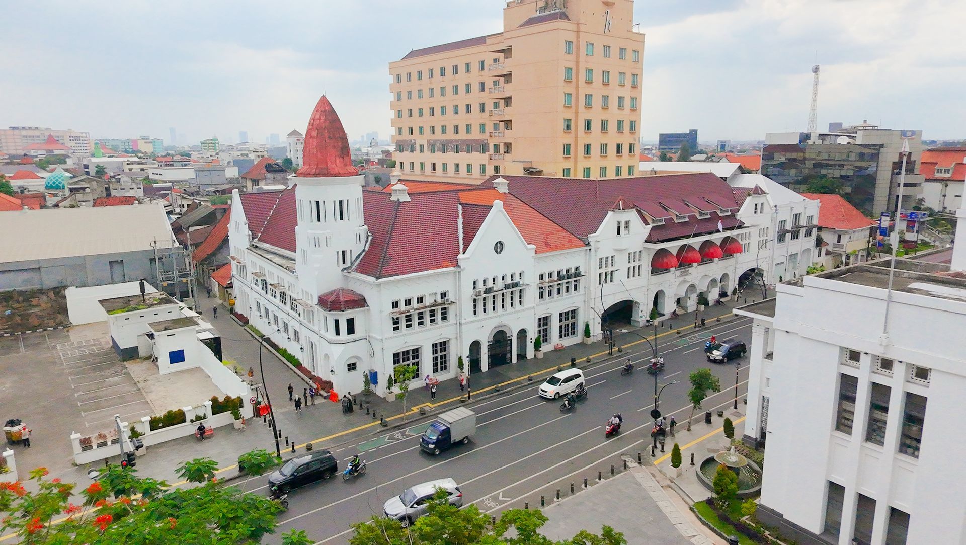 White colonial building with red roof, Semarang, Indonesia. Cars driving on road in front of the building.