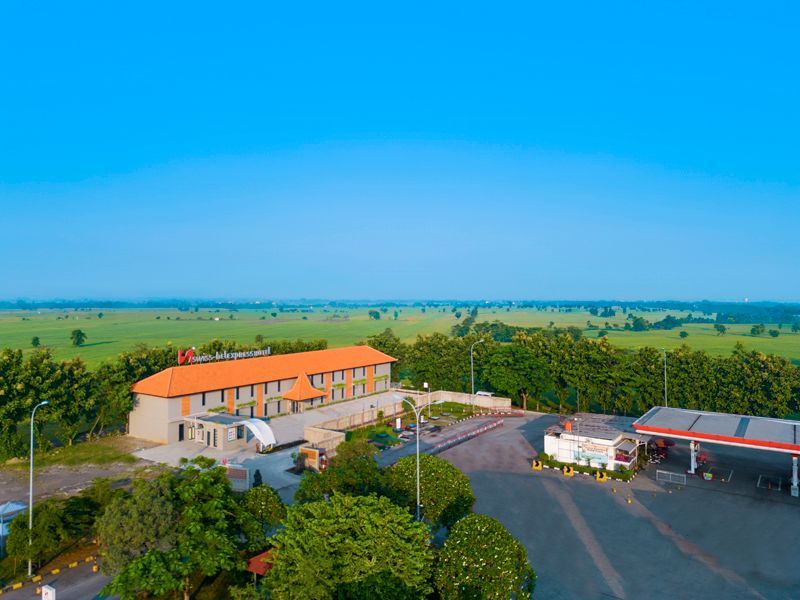 Aerial view of a rural building complex with orange roofs beside open farmland under a clear blue sky