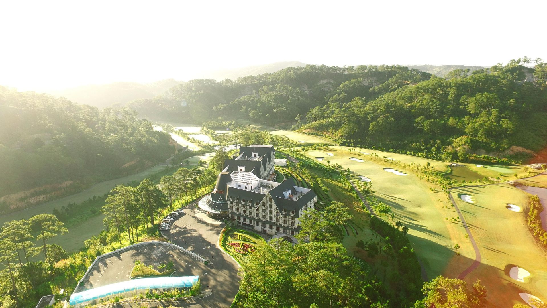 An aerial view of a grand building nestled amongst a golf course and lush green hills.