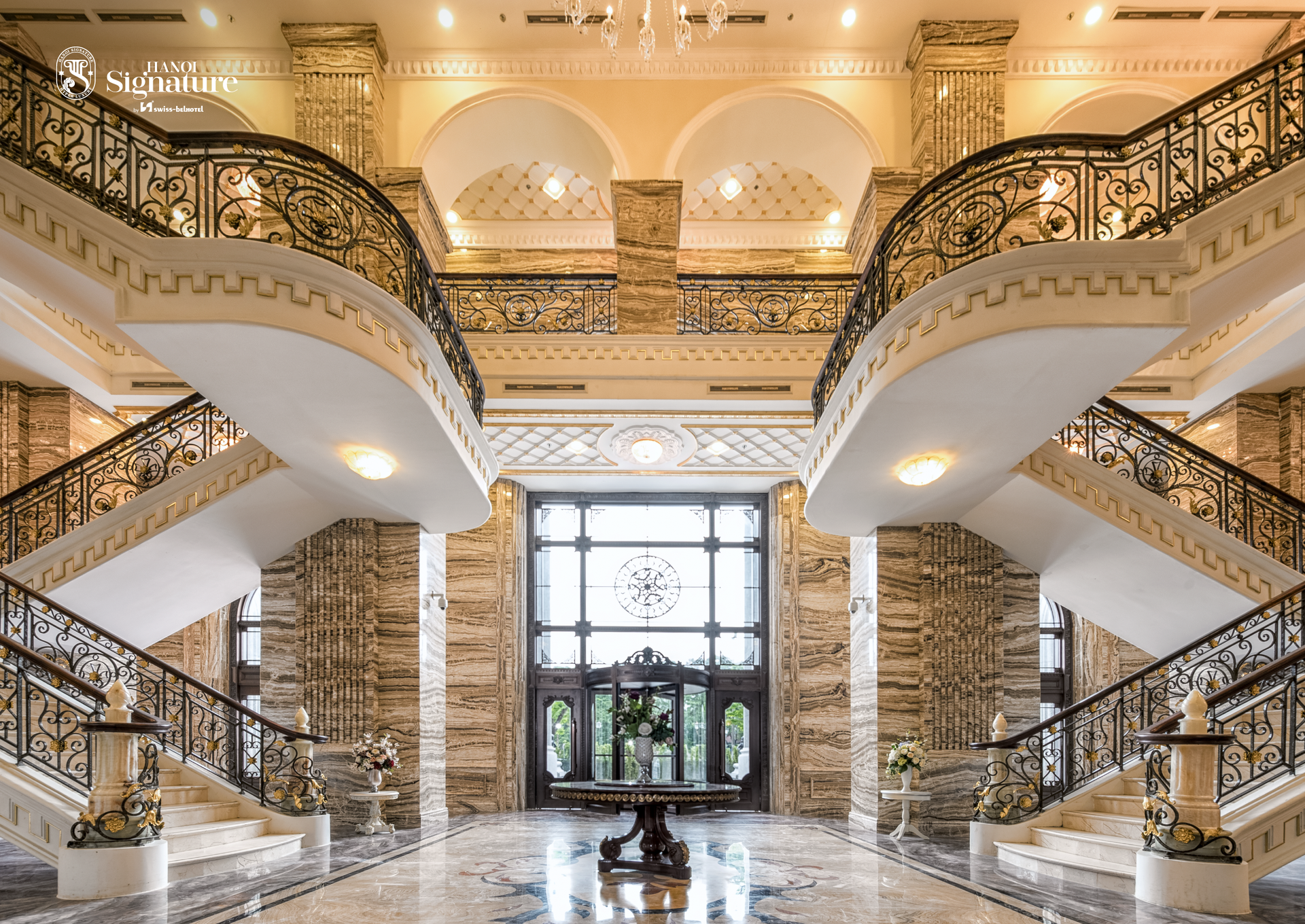 Grand entryway with marble and ornate staircase, leading to a large glass door.