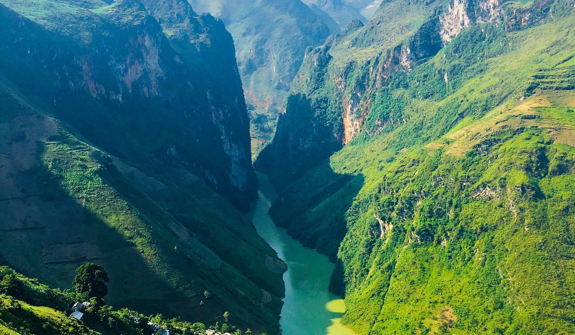 Green river winds through a deep, verdant canyon with towering rock walls.