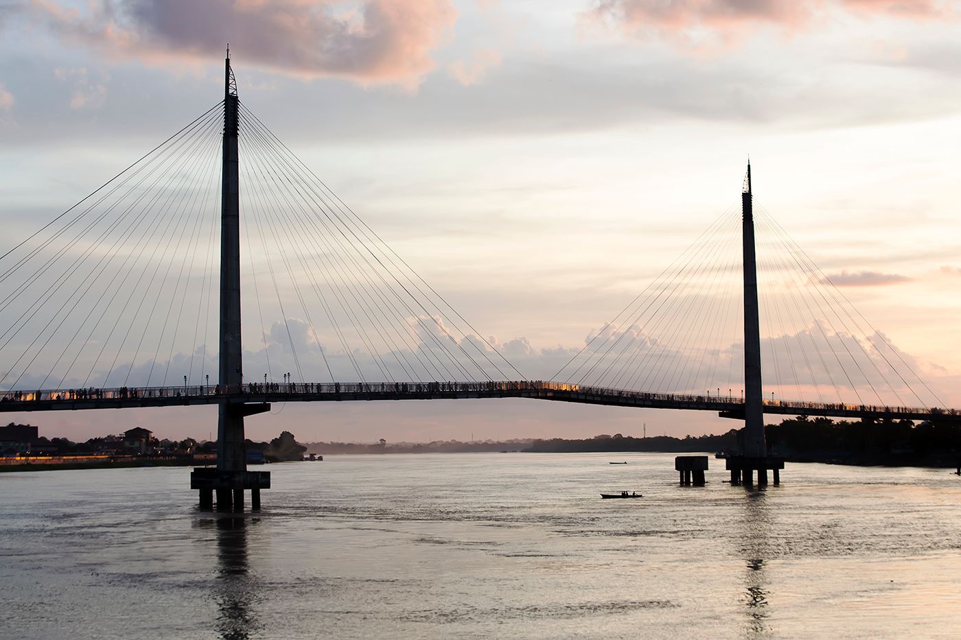 Cable-stayed bridge over water at sunset. Two towers support the bridge deck, against a cloudy sky.