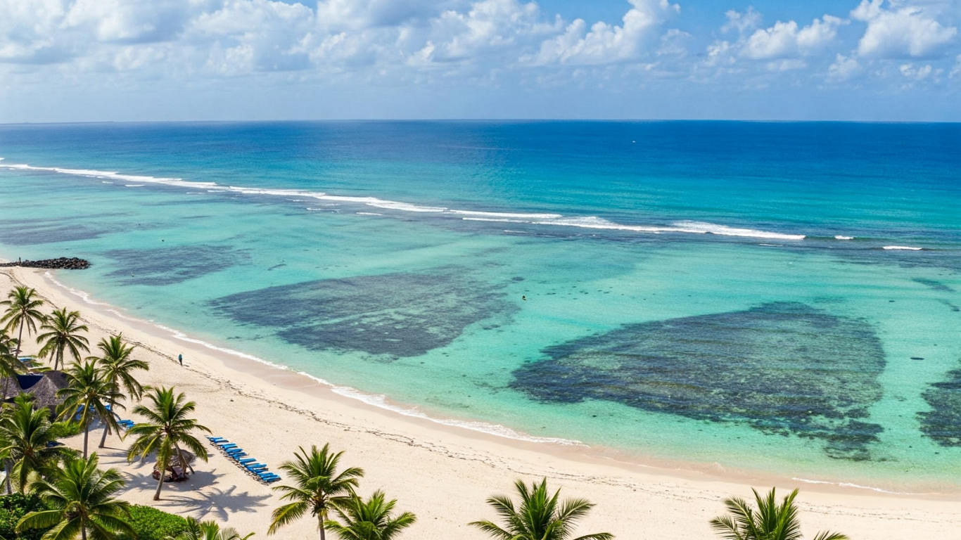 Vibrant turquoise ocean meets sandy beach, palm trees line the shore under a blue sky.