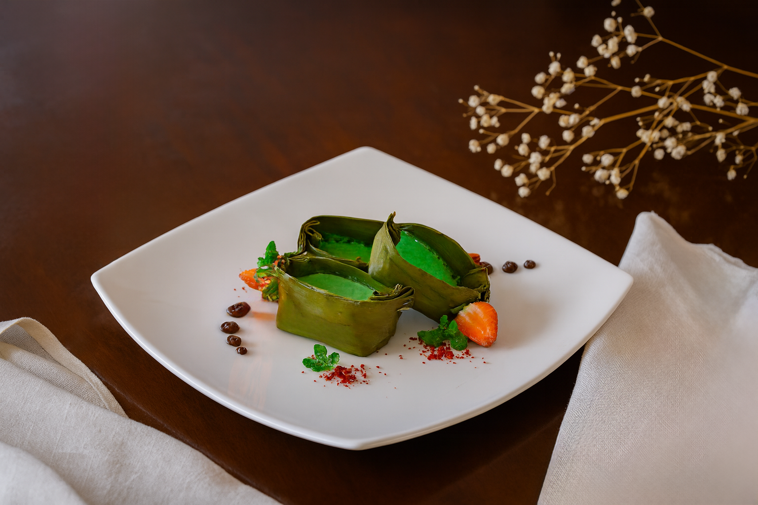 Green dessert in leaf-shaped containers on a white square plate, garnished with strawberries and herbs.